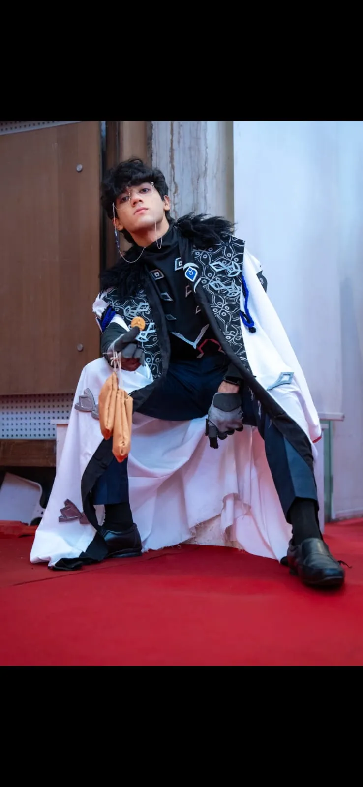 Cosplayer portraying Pantalone from Genshin Impact, wearing the signature Fatui Harbinger coat, glasses with chains, and holding a Mora pouch.