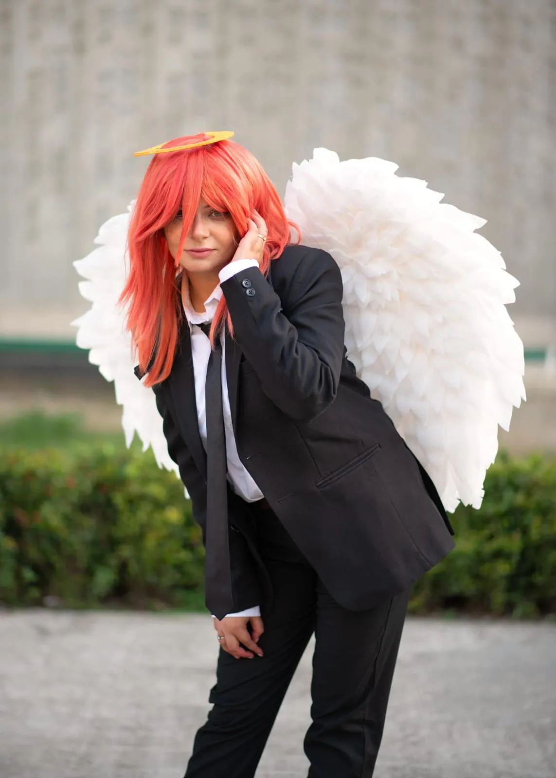 Cosplayer portraying the Angel Devil from Chainsaw Man anime, wearing the iconic Public Safety black suit, red hair, halo, and large white feathered wings.